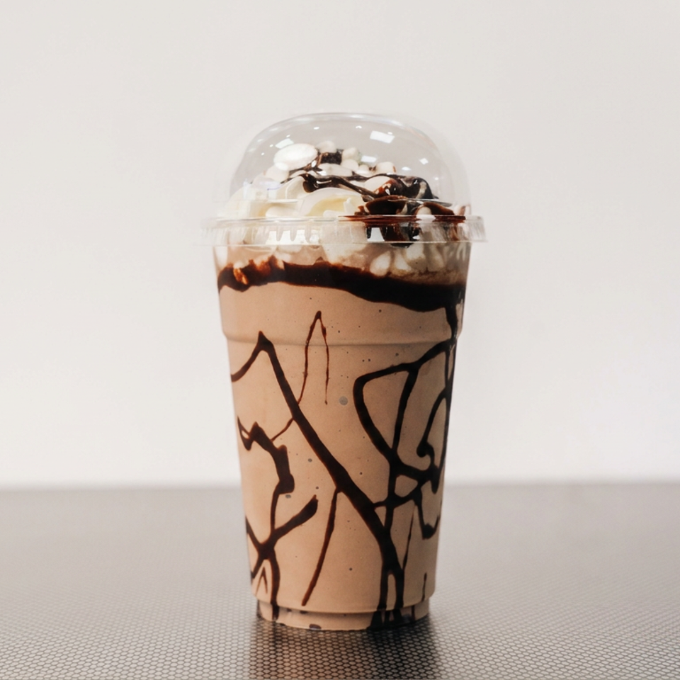 Chocolate milkshake topped with whipped cream and chocolate drizzle in a clear cup on a tabletop.