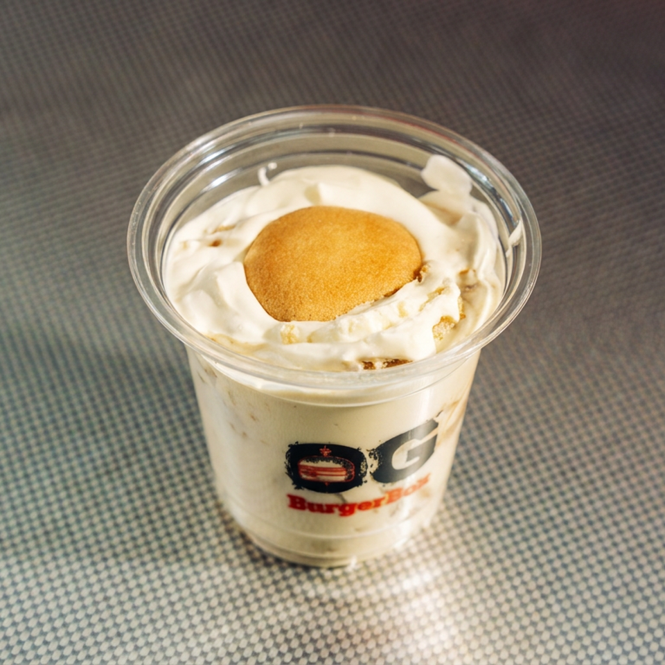 Clear cup of creamy dessert topped with whipped cream and a round golden cookie, displayed on a textured tabletop.