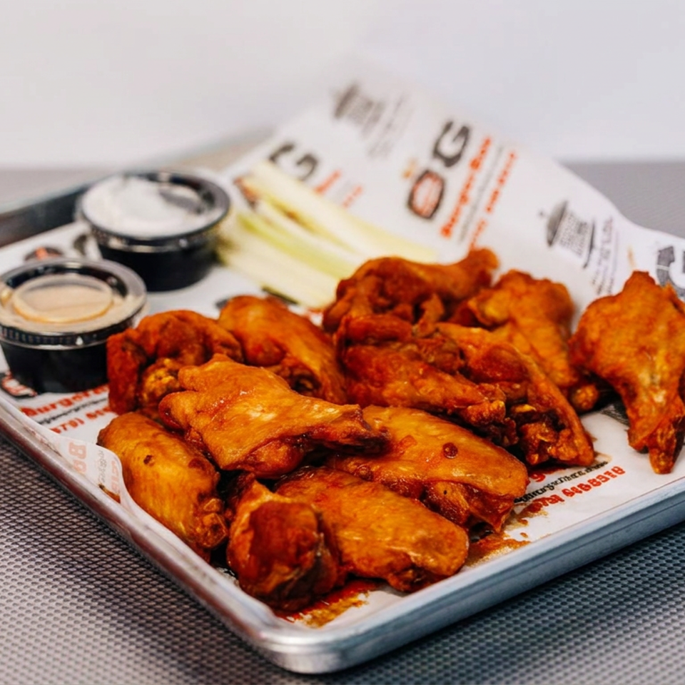 Tray of saucy chicken wings with dipping sauces and celery sticks on a restaurant-lined serving tray.